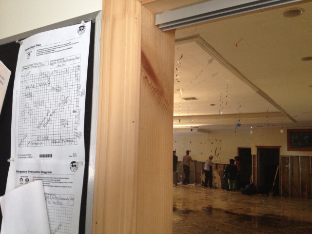 Emergency evacuation diagrams hang in the foreground as volunteers tear down moldy drywall in the church's events room.